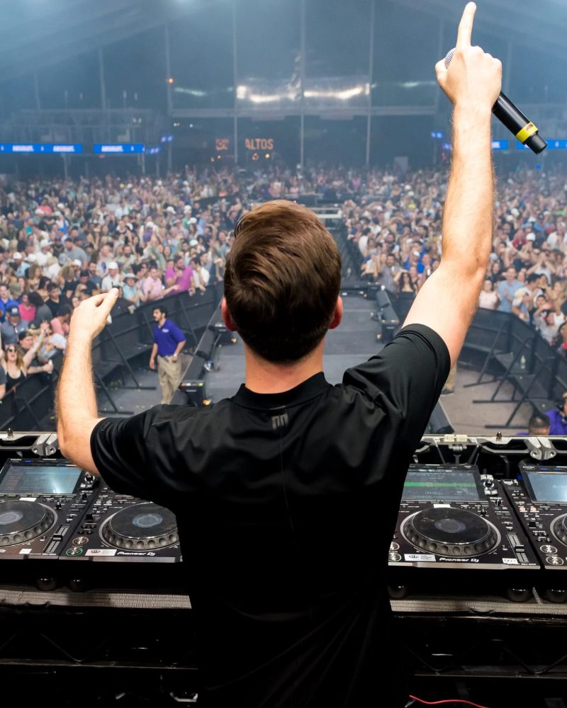 DJ with arm raised on stage in front of a packed crowd