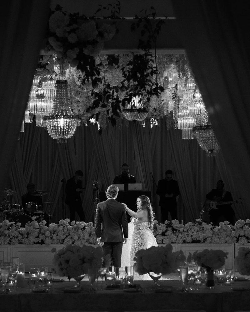 Couple’s first dance beneath crystal chandeliers, in black and white