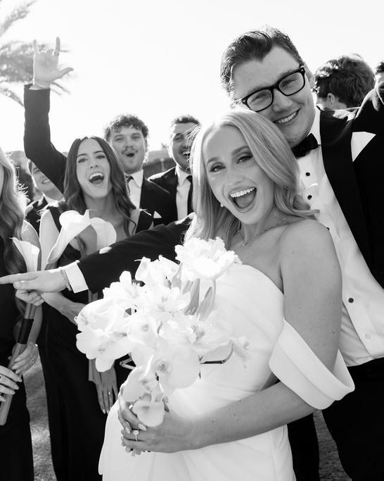 Bride laughing with her groom and wedding party, holding white calla lilies