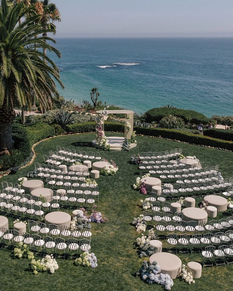 Oceanfront ceremony with curved rows of white chairs around a floral arch