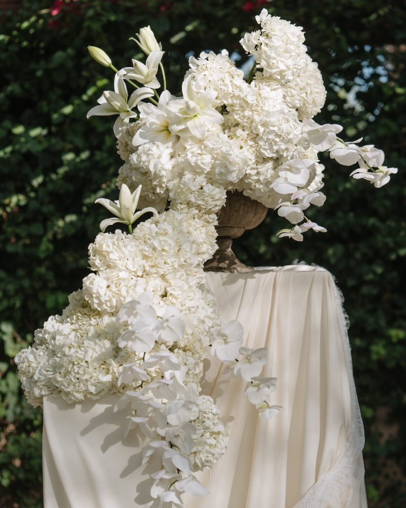 Tall white hydrangea and orchid arrangement on a draped pedestal