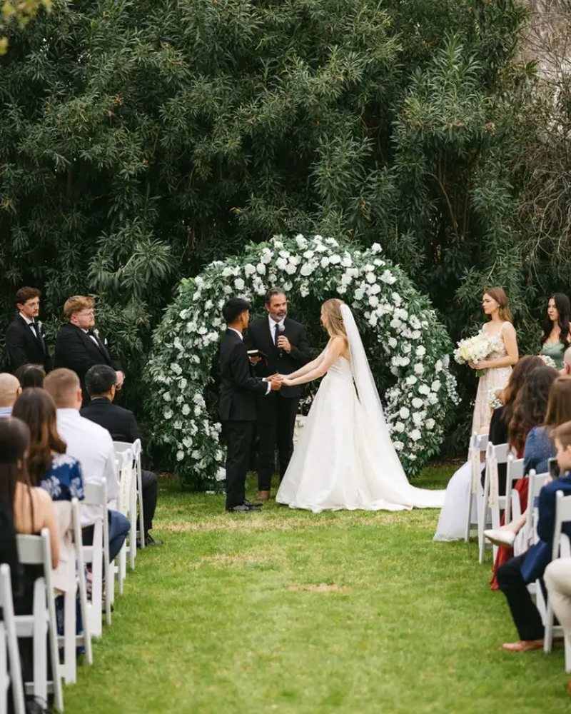 Couple exchanging vows in front of a white rose arch